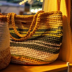 One crochet colored bag in focus standing on play wood plate indoor at exhibition stand, a warm yellow light-bulb light